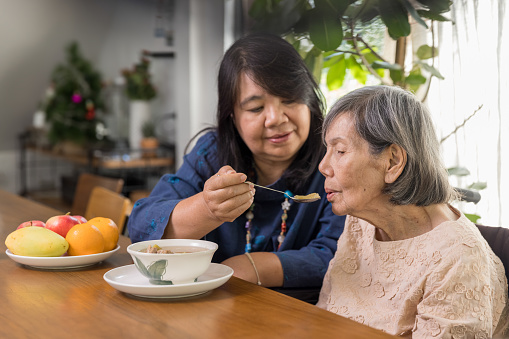 Daughter feeding elderly mother with soup.Senior asian woman bored with food.