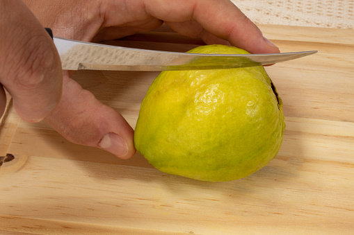 Hands holding guava being cut by knife. About rustic wooden board