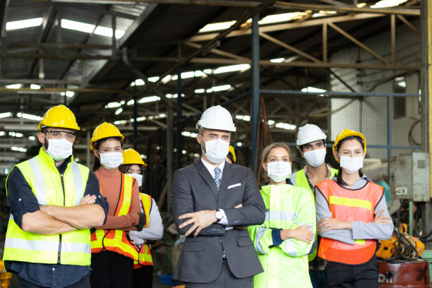 istock Large group of confident industrial engineer worker and foreman boss with face mask wearing safety equipment standing with arms crossed at manufacturing plant factory. 1294524127