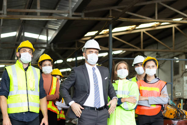 istock Large group of confident industrial engineer worker and foreman boss with face mask wearing safety equipment standing at manufacturing plant factory. 1294525025