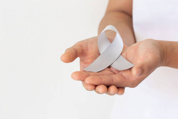 Hand holding Gray ribbon on white fabric background. Brain Cancer Awareness, Brain Tumors, Allergies, Asthma, Diabetes Awareness, Aphasia disease, Mental Illness Disorder. Healthcare medical concept. mano sosteniendo cinta gris sobre fondo de tela blanca. concientización sobre el cáncer cerebral, tumores cerebrales, alergias, asma, conciencia de la diabetes, enfermedad de la afasia, trastorno de enfermedades mentales. concepto médico de la salud.