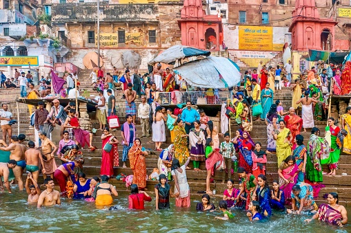 Varanasi, India - November 11, 2015. A large group of Indian religious pilgrims standing on a ghat and bathing in the Ganges River, a ritual in Hinduism. People appear happy and are wearing traditional clothing in vibrant colors.