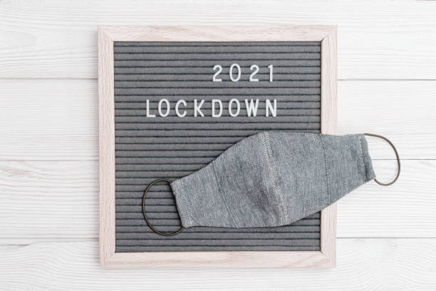 istock Grey colored Flatlay letter board with message text lockdown 2021 and protective face mask. Lock down loading concept. 1294536880