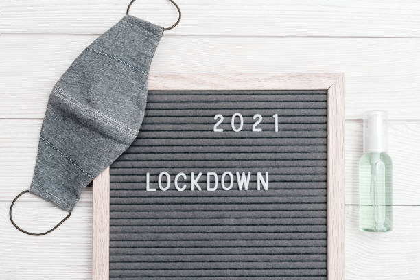 istock Flatlay letter board with message text lockdown 2021 and grey cloth protective face mask. Lock down loading concept. 1294536952