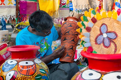 Kolkata, West Bengal, India - 31st December 2018 : Young Bengali artist man painting colors on terracotta pots, works of handicraft, for sale during Handicraft Fair in Kolkata.