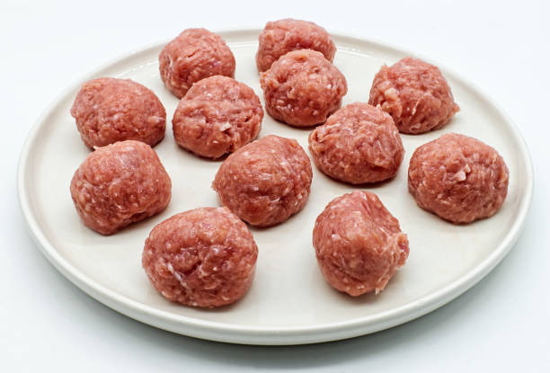 istock Raw meatballs with peas in a white dish isolated on white background. 1294544817