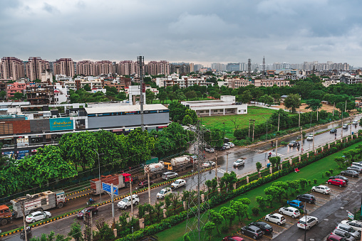 Gurugram, Haryana, India - 08.06.2019: Aerial view of busy streets and market area near a residential society with parked cars, green grass and trees. Gurgaon city skyline in rainy season.