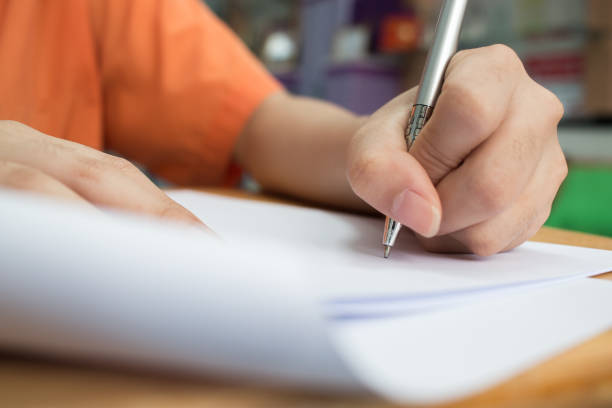 istock School Students hands taking exams, writing examination room with holding pencil on optical form of standardized test with answers and english paper sheet on desk doing final exam in classroom. 1294545937