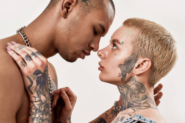 istock Multicultural relationship. A tattooed dark-skinned topless male looking down standing face to face with a white pierced tattooed woman hugging each other while she is looking into his eyes 1294548871