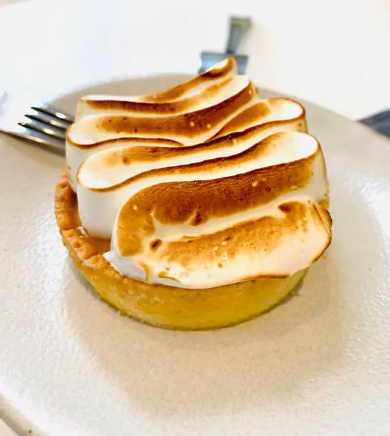 Close-up bird-eye-view image of vegan Lemon Meringue Tart, sweet dessert on a white plate.