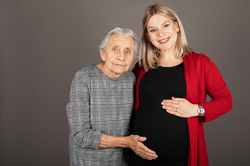 Studio portrait of pregnant cheerful woman hugging senior grandmother