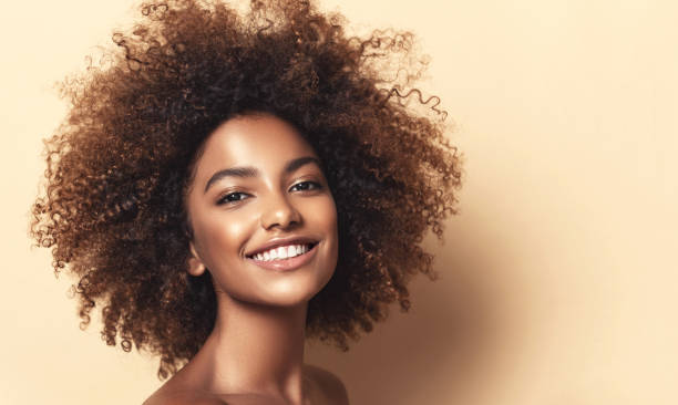 Shiny, toothy smile, and expression of gladness on the face of young brown skinned woman. Afro beauty. Shiny, toothy smile, and expression of gladness on the face of young, beautiful model with with vibrant, melanin-rich skin tone. Natural, dense afro hair on the head of brown skinned model. Sincere look at the viewer. coloring photos stock pictures, royalty-free photos & images