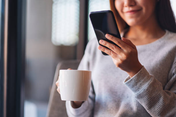 istock a beautiful young asian woman holding and using mobile phone while drinking coffee 1294561559