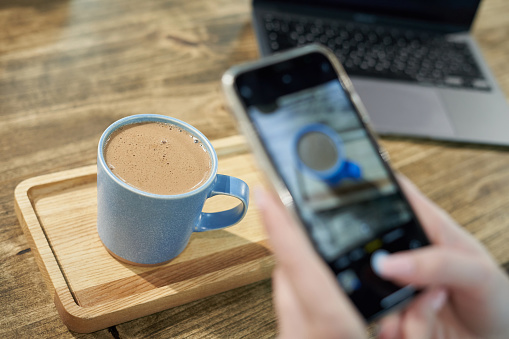 Person takes photos using smartphone of his coffee in mug for blogging