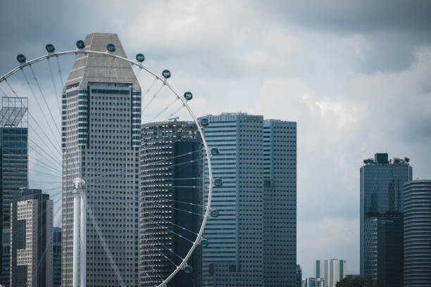 A ferris wheel in Singapore known as the Singapore Flyer. Behind it some high skyscrapers in the financial district of Singapore. Seen a cloudy day.