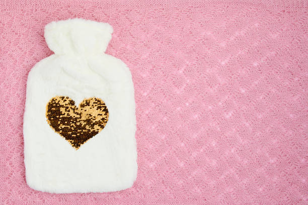 winter flat lay with hot water warmer on pink background.