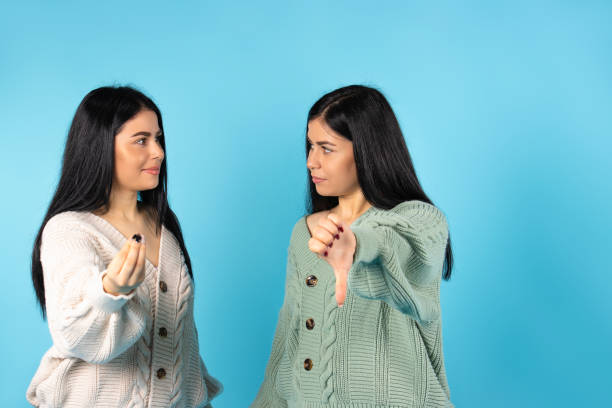 istock Two sisters are looking at each other against a blue background. One of them points a finger at a low-dislike. 1294570450