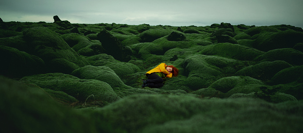 Panoramic shot of redhead sleeping in fetus position in fantasy and idyllic landscape in Icelandic moss