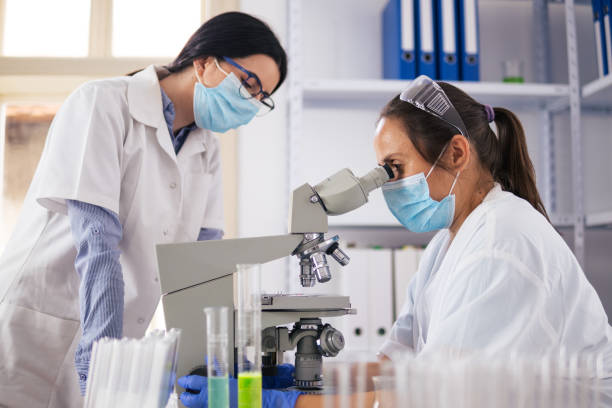 istock Coronavirus protection. Scientific researches in microbiological laboratory on COVID-19 vaccine elaboration in medical clinic. Female doctors wearing protective face masks looking at microbiology samples through a medical microscope and discussing. 1294572079