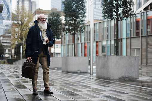 Happy business hipster elderly man walking to work with city on background - Focus face
