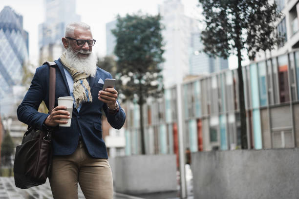istock Hipster senior business man using mobile phone app while drinking coffee while walking to work - Focus on face 1294575303