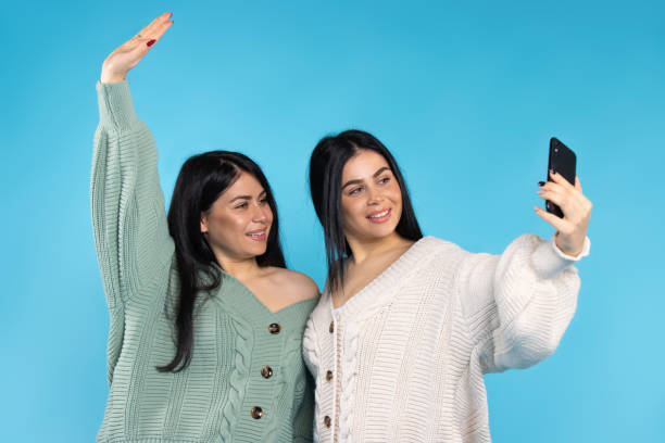 istock Cute brunette twins in the same clothes take a selfie on a blue background. Spending time together. 1294577197