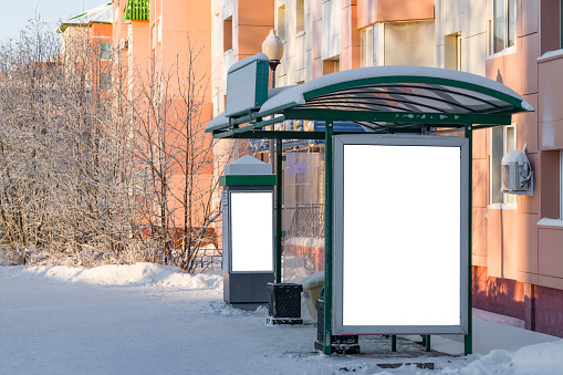 Billboard on the street at the bus stop in the city with empty white space for text on the background of trees, buildings in frost, snow, beautiful winter background,mockup