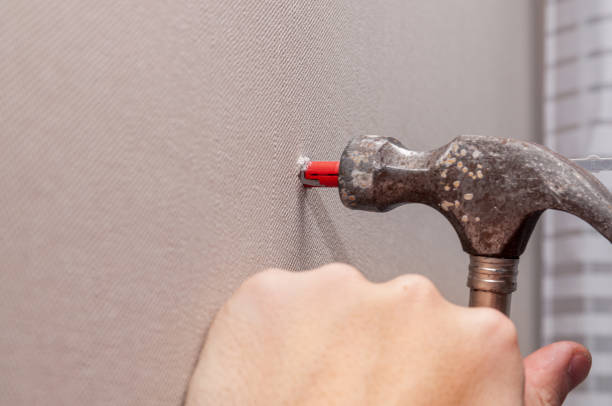 istock hammers a plastic dowel into a hole in the gray wall 1294580481