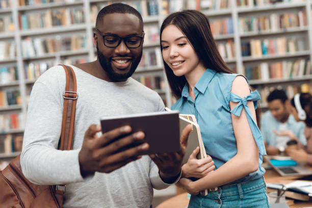 istock Group of ethnic multicultural students in library. Black guy and asial girl are using tablet. 1294582476