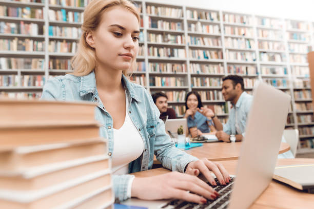 istock Group of ethnic multicultural students in library. White girl working on laptop. 1294582561