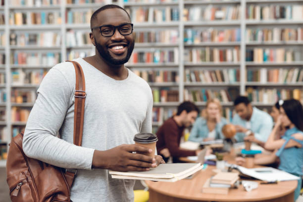 istock Group of ethnic multicultural students in library. Black guy with notes and coffee. 1294582704