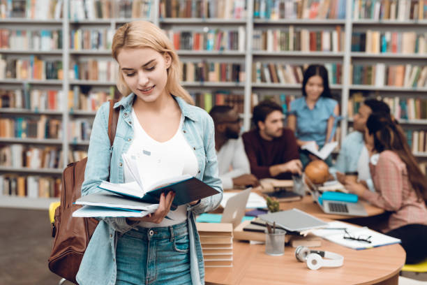istock Group of ethnic multicultural students in library. White girl reading book. 1294583303