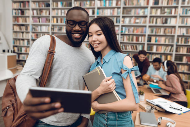 istock Group of ethnic multicultural students in library. Black guy and asial girl are using tablet. 1294583310