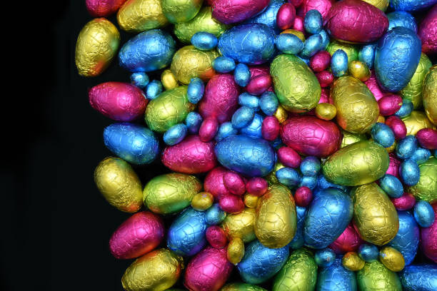 istock Pile or group of multi colored and different sizes of colourful foil wrapped chocolate easter eggs in pink, blue, yellow and lime green against a black background with copy space. 1294583471