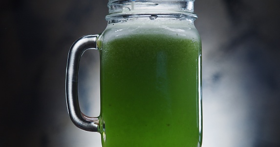 Pouring green smoothie into the drinking glass