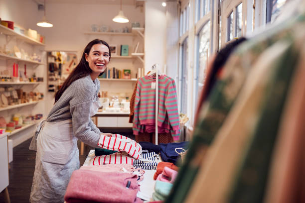 女性中小企業の所有者は、ウィンドウディスプレイに在庫を配置します - 店員 ストックフォトと画像