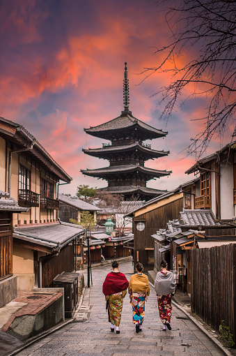 Kyoto, Japan, December 12, 2020. Three unidentified women wearing kimono are walking on the path leading to the to the Kiyomizu-dera Temple (defocused in the distance) during a stunning sunset. Kiyomizu-dera, formally Otowa-san Kiyomizu-dera, is a Buddhist temple in eastern Kyoto, Japan.