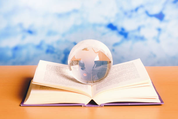 istock The world in a book: dreamy sky behind an open book with a glass crystal globe resting on it 1294586330