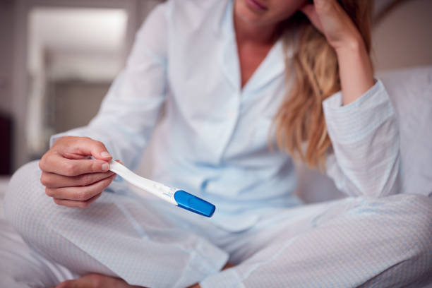 Close Up Of Unhappy Woman Wearing Pyjamas In Bedroom Holding Pregnancy Test Close Up Of Unhappy Woman Wearing Pyjamas In Bedroom Holding Pregnancy Test unwanted pregnancy stock pictures, royalty-free photos & images