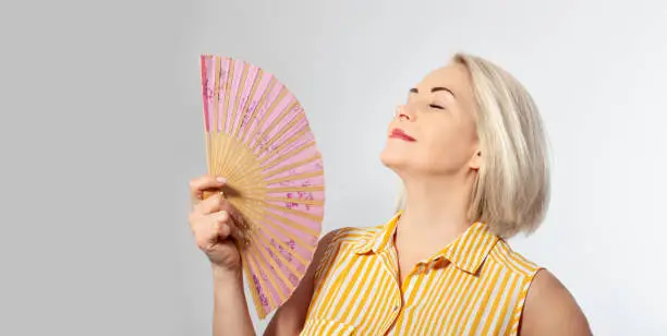 Photo of Attractive middle aged woman relaxing with fan. Mature woman experiencing hot flush from menopause isolated