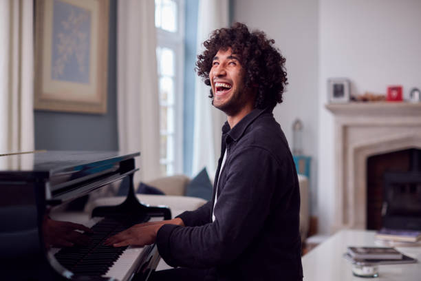 joven sentado en el piano de cola y tocando en casa - pianist grand piano piano playing fotografías e imágenes de stock