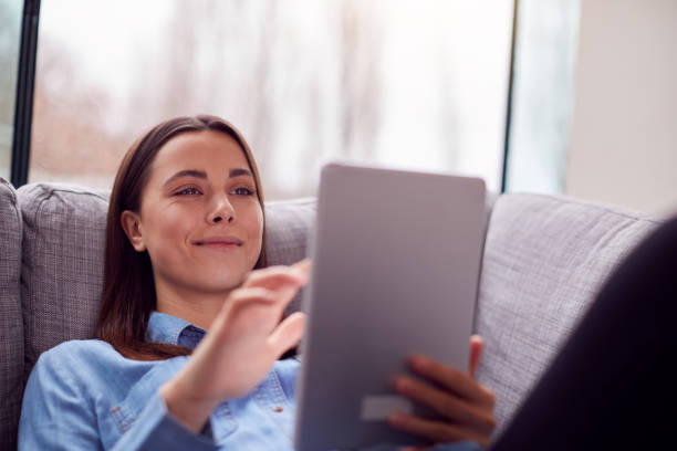 istock Smiling Young Woman At Home Lying On Sofa Looking At Digital Tablet 1294588085