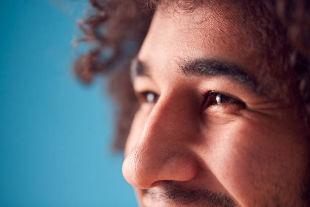 close up on eyes of smiling young man against blue background in studio - primary colours imagens e fotografias de stock