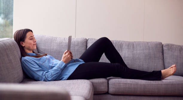 istock Smiling Young Woman At Home Lying On Sofa Looking At Digital Tablet 1294588756