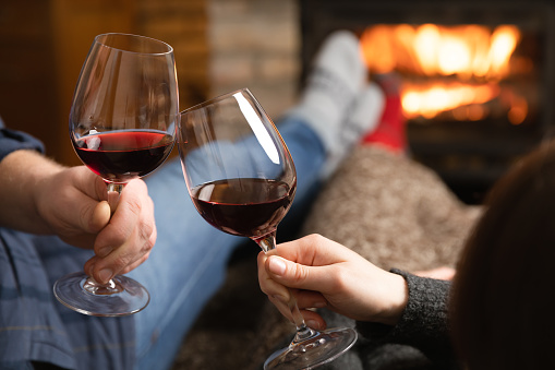 Couple in love sitting in a cozy room with fire place on a sofa with glass of wine. Family and love concept.