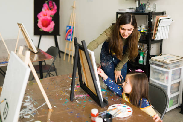 istock Female art teacher instructing a kid on how to use a paintbrush 1294592821