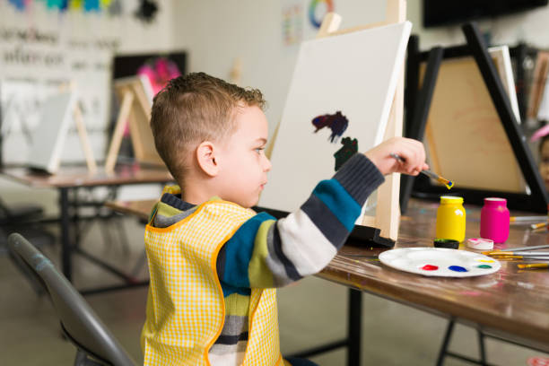 istock Rear view of an elementary kid painting with a brush on a canvas 1294593731