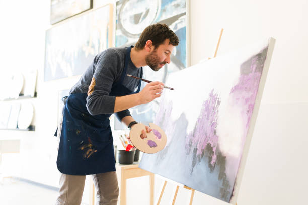 istock Side view of an hispanic man painting on a large canvas 1294596798
