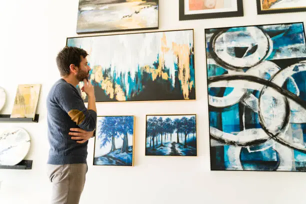 Photo of Hispanic guy is considering which painting to buy from the art gallery