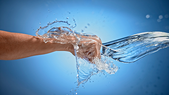 Close-up of woman's hand punching through the water against blue background.